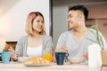 Happy asian couple in pajamas sitting at table in kitchen at home in morning and having cereal breakfast together