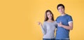 Happy Asian couple pointing fingers at empty copy space for text over yellow background Royalty Free Stock Photo