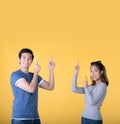 Happy Asian couple pointing fingers up at empty copy space for text over yellow background Royalty Free Stock Photo