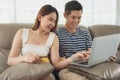 Happy asian couple shopping online using digital tablet with holding credit card and sitting on sofa at home together.
