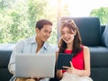 Happy Asian couple, young man and woman looking digital tablet screen while using laptop computer. Royalty Free Stock Photo