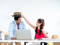 Happy Asian couple, young woman put hat on man head with smile while using laptop computer. Royalty Free Stock Photo