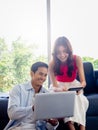 Happy Asian couple, young woman sit on sofa and man on floor looking and using laptop computer. Royalty Free Stock Photo