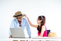 Happy Asian couple, young woman put hat on man head with smile while using laptop computer on desk together. Royalty Free Stock Photo