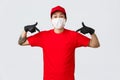 Happy asian delivery guy in red uniform, cap and t-shirt, wearing protective gloves and mask during covid19 quarantine