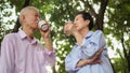 Happy Asian elderly couple morning walk in green city while drin Royalty Free Stock Photo