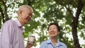 Happy Asian elderly couple morning walk in green city while drin