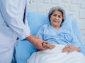 Happy Asian elderly patient woman smiling on bed while doctor in white lab coat holding hand for check to examine heartbeat pulse. Royalty Free Stock Photo