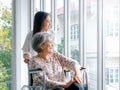 Happy Asian elderly woman, mother or grandparents on wheelchair taking care by caregiver, smiling young female.