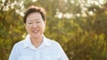 Happy Asian elderly woman smiling in morning sun with green back