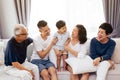 Happy Asian extended family sitting on sofa together, posing for group photos.