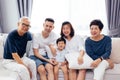 Happy Asian extended family sitting on sofa together, posing for group photos.