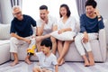 Happy Asian extended family sitting on sofa together and watching little child playing toy on the floor with happiness.