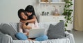 Happy asian famile with laptop sitting on couch young korean mum playing piggybacking with little funny kid daughter