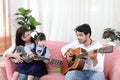 Happy Asian family. Chubby little girl daughter learning to play acoustic guitar with her dad. Child with mother and father Royalty Free Stock Photo