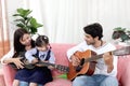 Happy Asian family. Chubby little girl daughter learning to play acoustic guitar with her dad. Child with mother and father Royalty Free Stock Photo