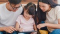 Happy Asian family dad, mom and daughter using computer tablet technology sitting sofa in living room at house. Self-isolation, Royalty Free Stock Photo