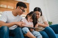 Happy Asian family dad, mom and daughter using computer tablet technology sitting sofa in living room at house. Self-isolation, Royalty Free Stock Photo