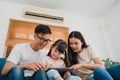 Happy Asian family dad, mom and daughter using computer tablet technology sitting sofa in living room at house. Self-isolation, Royalty Free Stock Photo