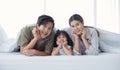 Happy Asian family with a daughter are lying and Putting hand on chin under the blanket on bed in the bedroom Royalty Free Stock Photo