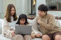 Happy asian family father mother and child daughter having fun using laptop computer sitting on couch in living room at home. Royalty Free Stock Photo