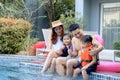 Happy Asian family, father mother daughter and son enjoy outdoor activity at swimming pool, kid and parent sitting by blue water Royalty Free Stock Photo