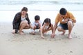 Happy asian family father and mother playing with their children boy and girl, they playing and writing something on sandy beach Royalty Free Stock Photo