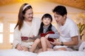 Happy asian family father and mother sitting teaching play ukulele guitar with daughter together on bed. Royalty Free Stock Photo