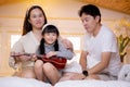 Happy asian family father and mother sitting teaching play ukulele guitar with daughter together on bed. Royalty Free Stock Photo