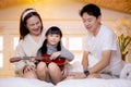Happy asian family father and mother sitting teaching play ukulele guitar with daughter together on bed. Royalty Free Stock Photo