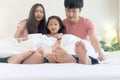Happy Asian family has fun in bedroom. Feet of mother, father and daughter lying in bed together and hiding under white blanket. Royalty Free Stock Photo