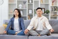 Happy asian family at home on sofa meditating, couple man and woman sitting in lotus position in living room with closed Royalty Free Stock Photo