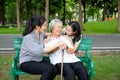 Happy asian family in outdoor park,smiling senior woman sitting on a bench while her daughter and granddaughter are hugging her, Royalty Free Stock Photo