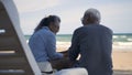 Happy Asian family, senior couple sitting on chairs with backs on beach travel vacation talking together Royalty Free Stock Photo