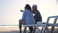 Happy Asian family, senior couple sitting on chairs with backs on beach travel vacation talking together Royalty Free Stock Photo