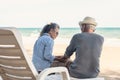 Happy Asian family, senior couple sitting on chairs with backs on beach travel vacation talking together Royalty Free Stock Photo