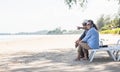 Happy Asian family, senior couple sitting on chairs with backs on beach travel vacation talking together Royalty Free Stock Photo