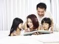 Asian family with two children reading book in bed Royalty Free Stock Photo