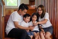 happy asian Family watching video on mobile phone at home together. father,mother ,son,daughter using smartphones on stair. Royalty Free Stock Photo