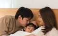 Happy Asian family, young father, mother, cute daughter sleeping together on bed in bedroom at home. Young parent kissing and lull Royalty Free Stock Photo