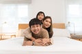 Happy Asian family, young mother, father, little cute daughter lying, playing, having fun together on bed in bedroom at home, Royalty Free Stock Photo