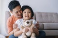 Happy Asian father and daughter playing together in the living room at home. The cute little girl hug the doll and smile happily