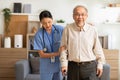 Happy asian female doctor helping elderly patient walking with cane or walking stick at home.Nures or caregiver assistance and