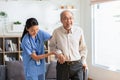 Happy asian female doctor helping elderly patient walking with cane or walking stick at home.Nures or caregiver assistance and