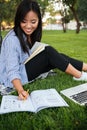 Happy asian female student in striped shirt writing to notebook, while studying in park, outdoor Royalty Free Stock Photo