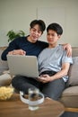 A happy Asian gay man enjoys watching a movie through a laptop with his boyfriend on a couch Royalty Free Stock Photo
