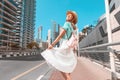 Happy Asian girl in a dress walks through a modern neighborhood with skyscrapers and office buildings. Tour and travel in Dubai Royalty Free Stock Photo