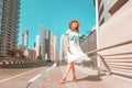 Happy Asian girl in a dress walks through a modern neighborhood with skyscrapers and office buildings. Tour and travel in Dubai Royalty Free Stock Photo