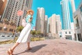 Happy Asian girl in a dress walks through a modern neighborhood with skyscrapers and office buildings. Tour and travel in Dubai Royalty Free Stock Photo