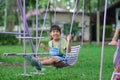 Happy Asian girl having fun playing in the playground during summer. Cute little girl swinging in the playground with a smile and